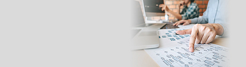 Ein Mann sitzt vor einem Schreibtisch und zeigt mit der Hand auf ein Papier mit einer Analyse.