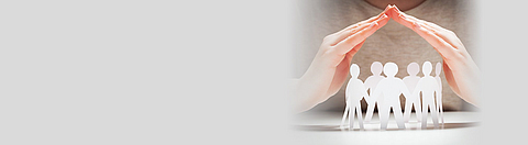 Schützende Hände über einer aus Papier ausgeschnittenen Gruppe