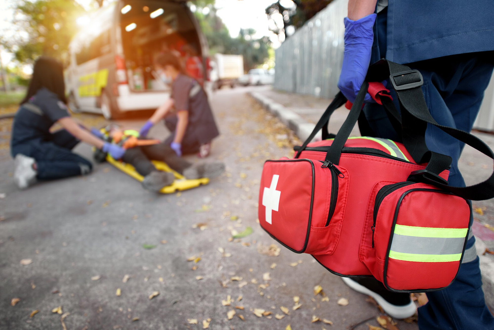 Zwei Rettungssanitäter versorgen eine verletzte Person und eine weitere bringt eine Tasche mit medizinischen Hilfsmitteln