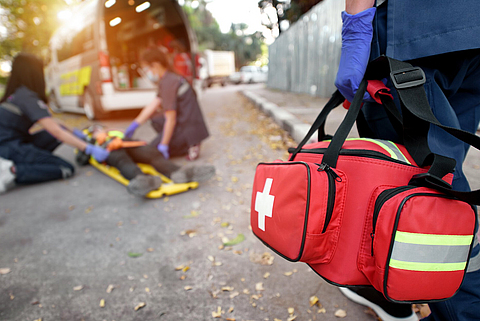 Zwei Rettungssanitäter versorgen eine verletzte Person und eine weitere bringt eine Tasche mit medizinischen Hilfsmitteln