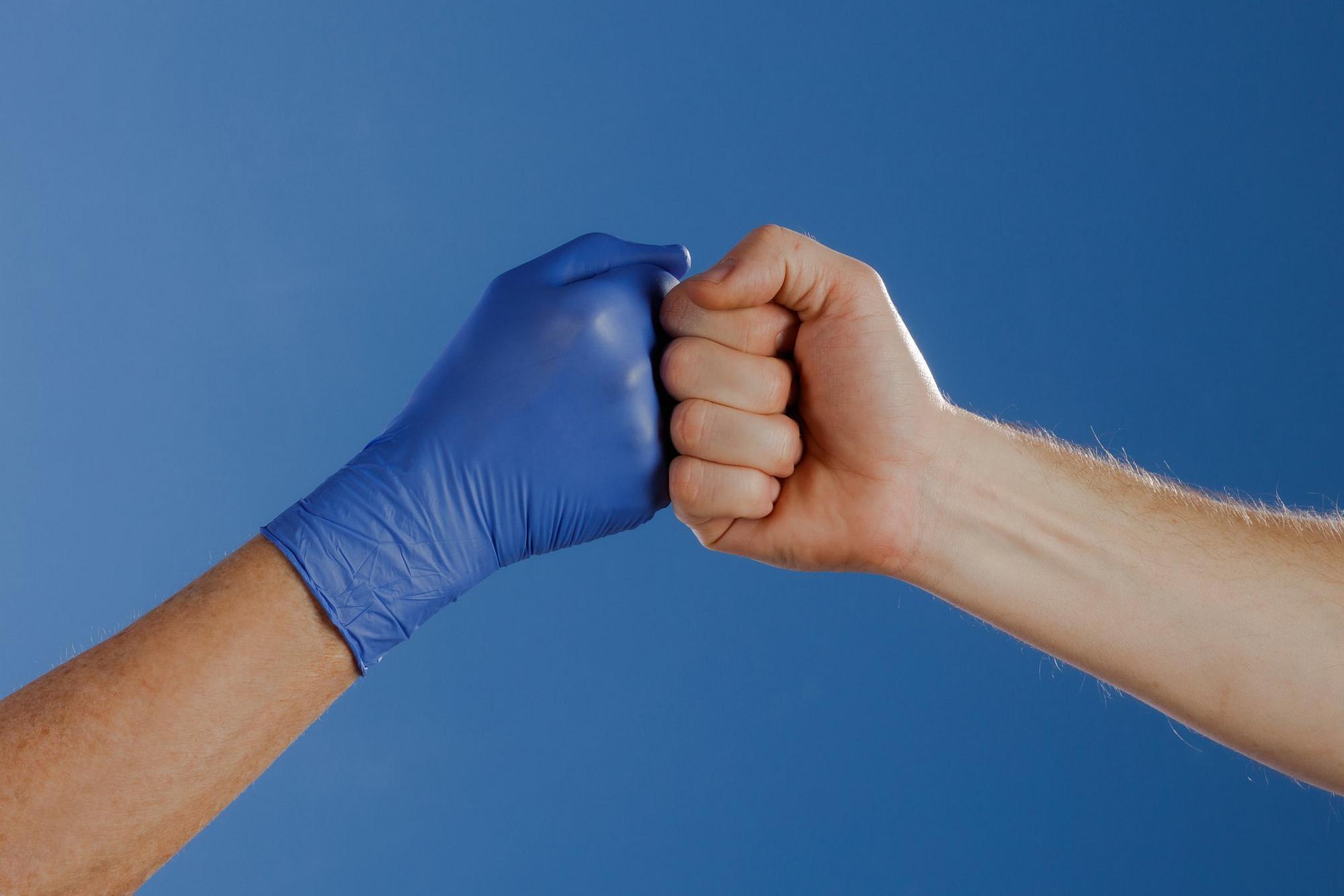 Zwei Männer machen einen Faustschlag eine Hand hat ein blauen Latexhandschuh an und einer nicht