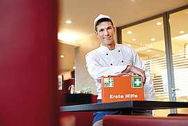 Ein junger Koch zeigt einen Erste-Hilfe-Kasten