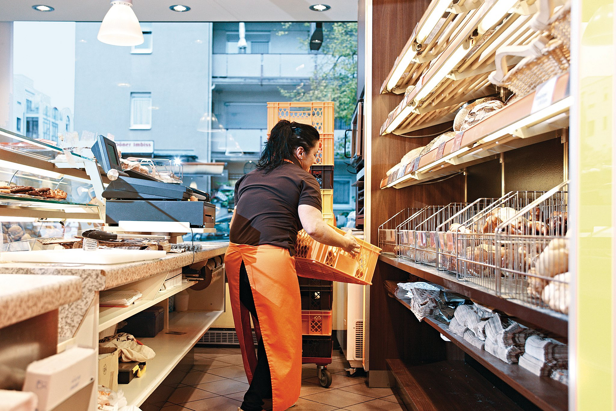 Bäckereiverkäuferin hebt hinter der Verkaufstheke eine Brotkiste hoch