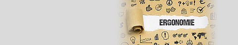 Auf Kraftpapier sind mit schwarzem Stift verschiedene Symbole rund um den Begriff Ergonomie gezeichnet, der in der Mitte auf weißem Hintergrund steht