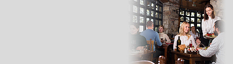 Gäste sitzen im Restaurant und reden mit einer Servicekraft