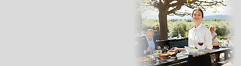 Servicekraft bringt Lebensmittel an einen Tisch im Außenbereich eines Restaurants.