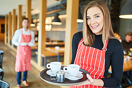 Junge Kellnerin trägt ein Tablett mit Kaffeetassen