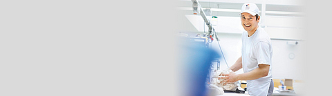 Ein Bäcker knetet Teig und lacht in die Kamera.