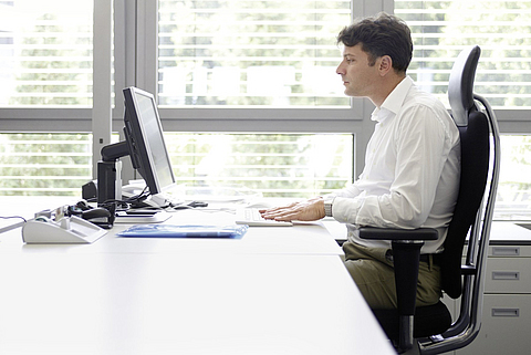 Mann sitzt am Schreibtisch vor dem Computer