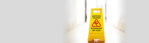 Ein Warnschild mit "Achtung Rutschgefahr" steht in einem Gang.