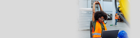 Frau sitzt auf einem Stuhl, streckt die Arme hoch und dehnt sich.